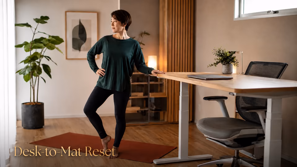 Woman beginning a hip mobility flow beside a standing desk after sitting during the workday